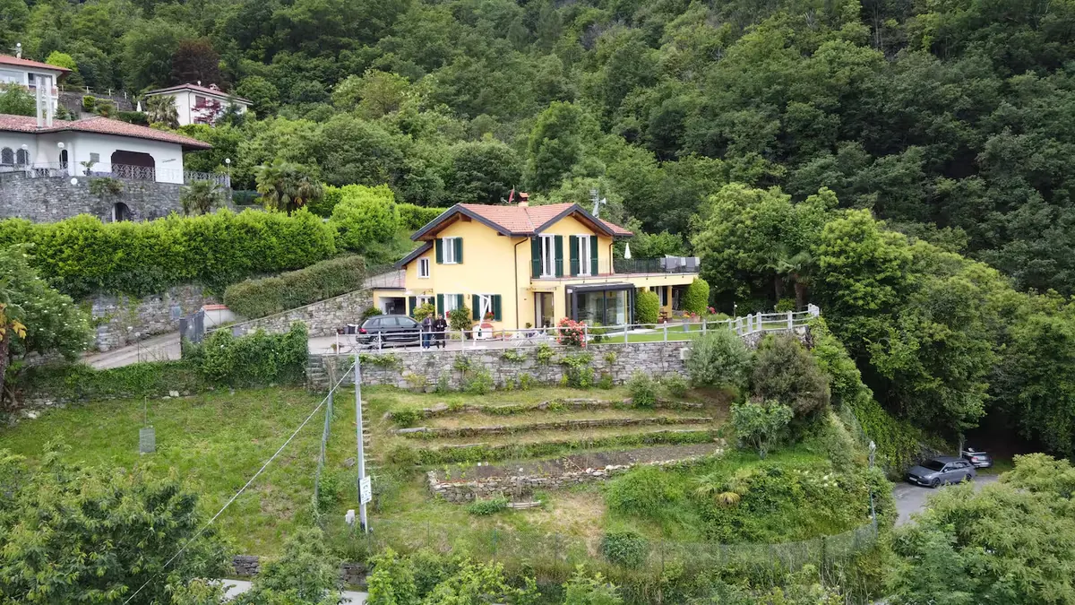 Veduta aerea di Casa Edenrock, con il giardino terrazzato, la strada tornante e il bosco che scende verso il lago