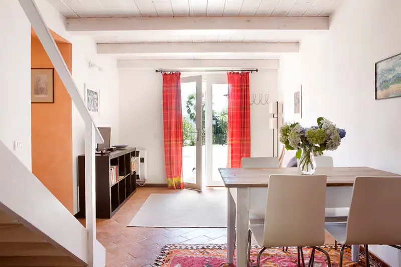 Sala da pranzo dell'appartamento con travi a vista, tavolo in legno, scala interna e porta finestra sul giardino