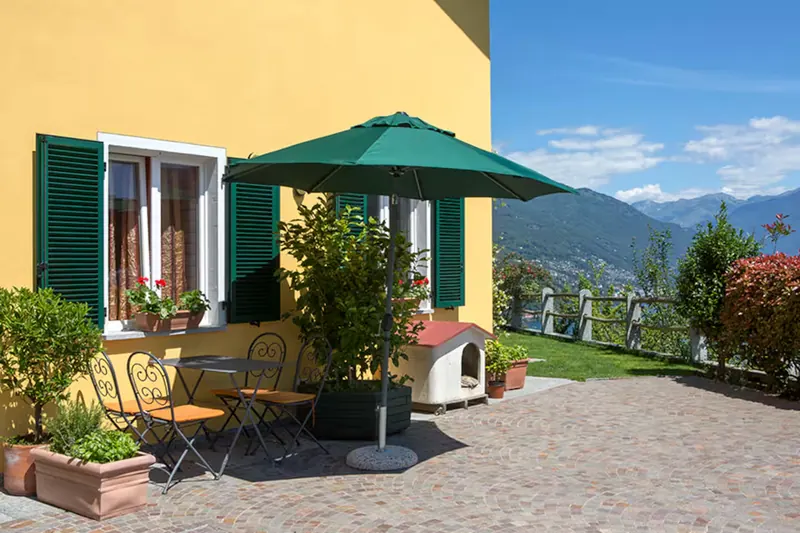 La terrazza di Casa Edenrock con ombrellone verde, tavolo apparecchiato e il forno in pietra, sulla facciata gialla della casa