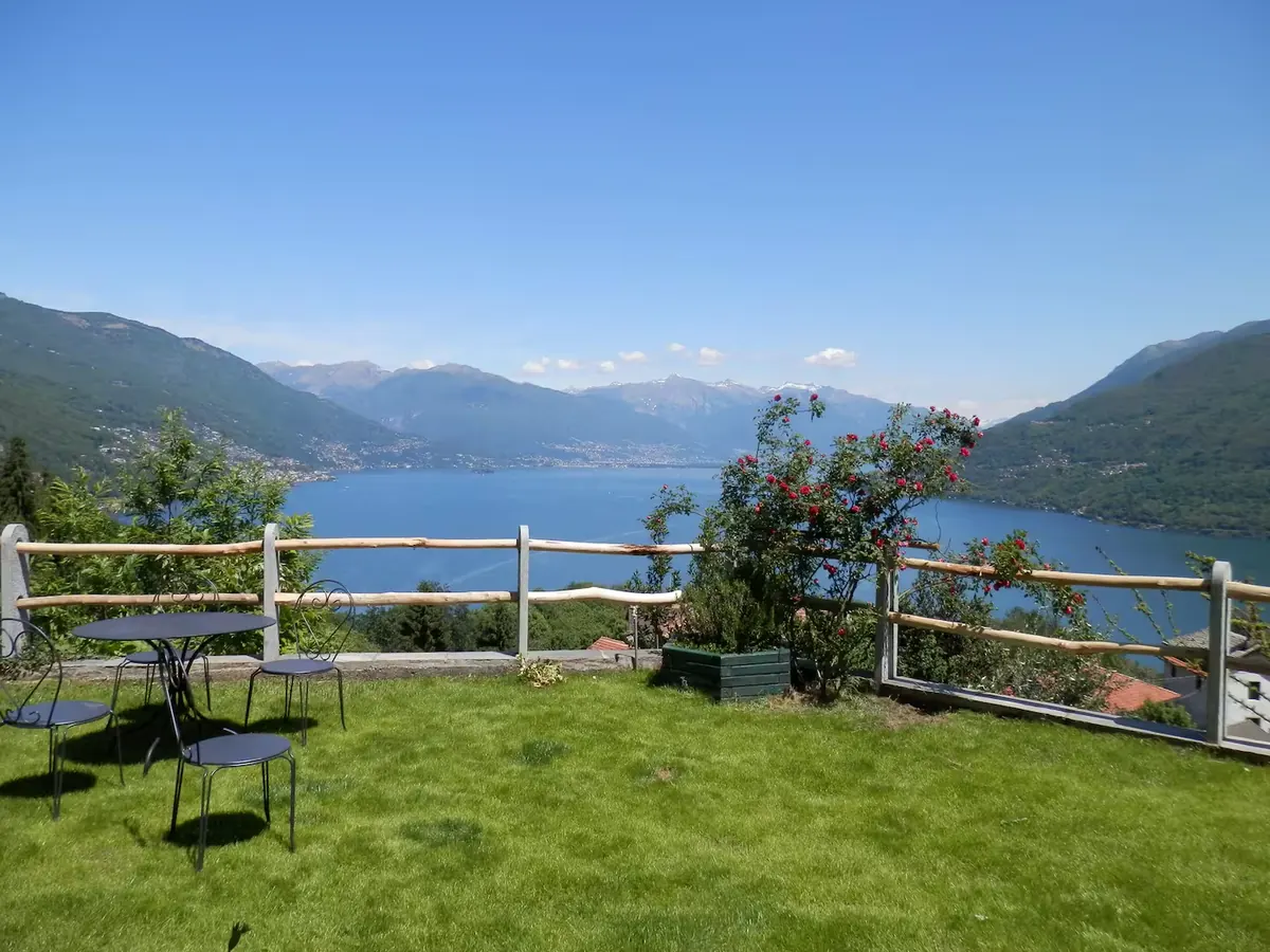 Il giardino di Casa Edenrock con tavolo e sedie, la staccionata in legno e il Lago Maggiore con le montagne sullo sfondo
